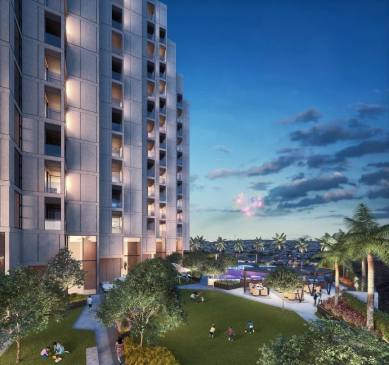 Vista panorámica al atardecer de las amplias amenidades exteriores de Adamant Grand León, mostrando la alberca, áreas verdes, zonas de descanso, paisajismo tropical y la base del edificio residencial. Personas disfrutan de los espacios.