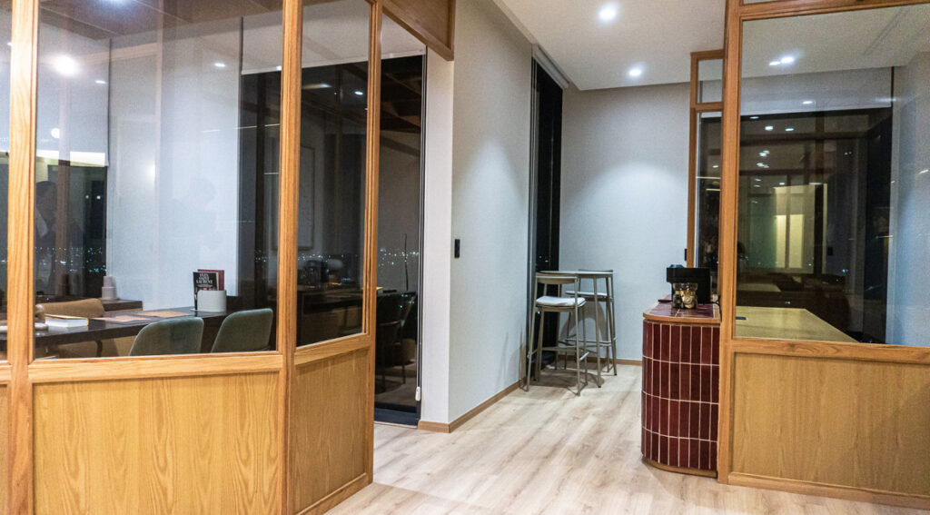 Vista del pasillo que conecta las oficinas privadas y áreas de descanso del coworking en Level Campestre León, destacando las divisiones con madera y cristal.