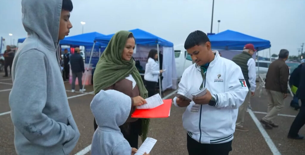 Una familia migrante integrada por una mujer y dos menores recibe información y documentos de un agente del programa Héroes Paisanos en un punto de revisión fronteriza durante su regreso a México.