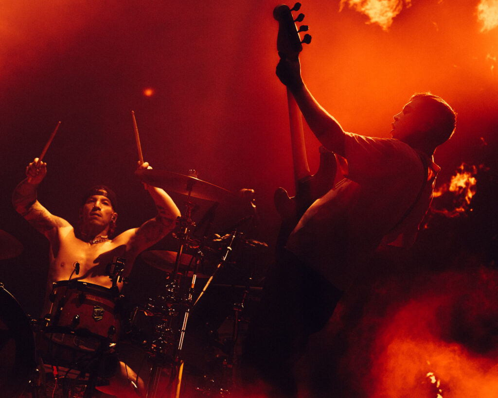 Josh Dun (baterista) y Tyler Joseph (bajista) de Twenty One Pilots en un concierto intenso con luces rojas y humo, durante la grabación de su película en la Ciudad de México.