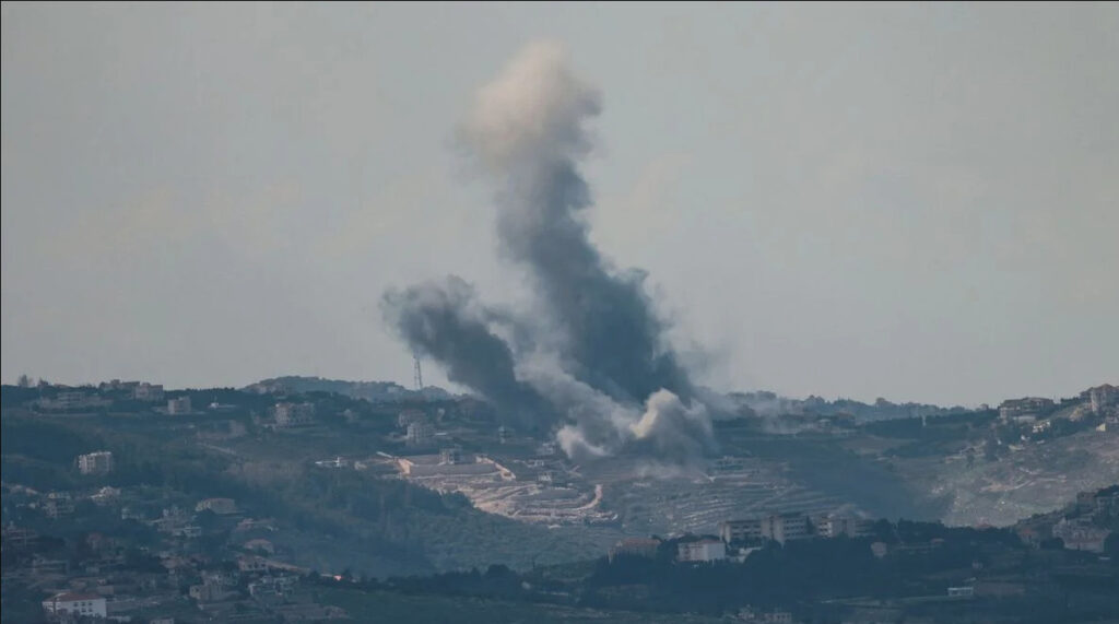 Vista panorámica a distancia de una zona montañosa y poblada bajo un cielo brumoso, donde una gran columna de humo gris y blanco se eleva tras un ataque aéreo reciente. Pequeños edificios de aldeas son visibles en las laderas. Foto por AFP.