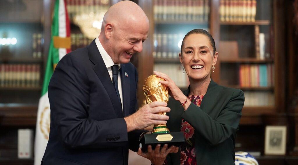 La presidenta de México Claudia Sheinbaum y el presidente de la FIFA Gianni Infantino sosteniendo juntos el trofeo de la Copa del Mundo en un despacho oficial.