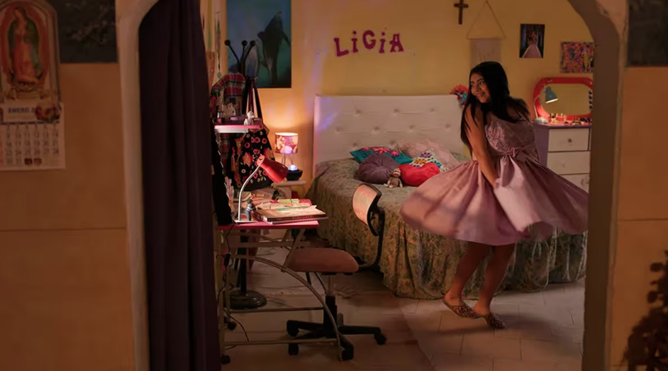 Escena de la película 'Quince' donde una joven con vestido rosa gira en su habitación decorada, mostrando un ambiente íntimo y cotidiano.