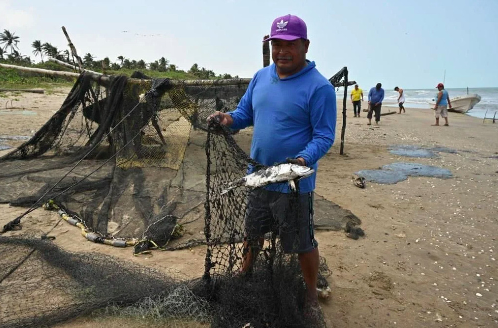 Un pescador del pueblo de Paylebot, Tabasco, muestra un pez cubierto de petróleo y redes de pesca dañadas por el derrame de hidrocarburos en la playa.Foto: Reforma.
