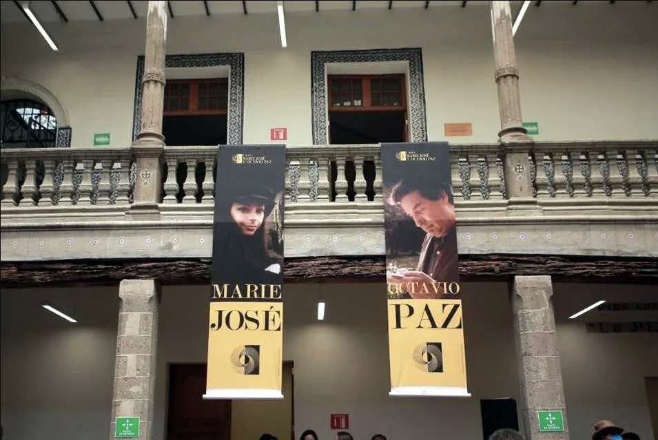 Fotografía del patio interior de la Casa Marie José y Octavio Paz con dos pendones colgantes: uno con el retrato de Marie José y otro con el de Octavio Paz.