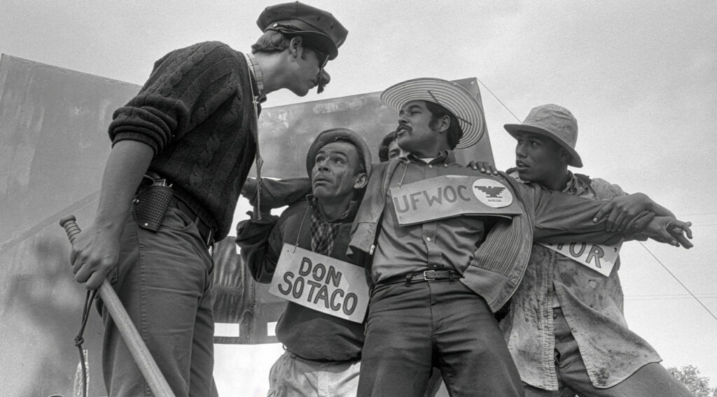 Fotografía en blanco y negro de una representación teatral del Teatro Campesino con actores personificando a 'Don Sotaco' y miembros del UFWOC, capturada en el documental American Pachuco.
