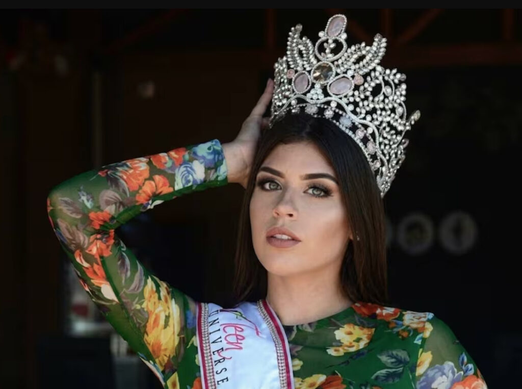 Retrato de Carolina Flores Gómez con una corona de reina de belleza, banda de Miss Teen Universe y vestido floral de manga larga.