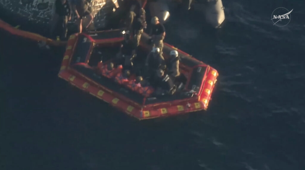 Vista aérea de una balsa inflable hexagonal de color naranja y negro, conocida como portón delantero, con varios astronautas y personal de rescate de la NASA en el mar tras el amerizaje de la cápsula Orión.