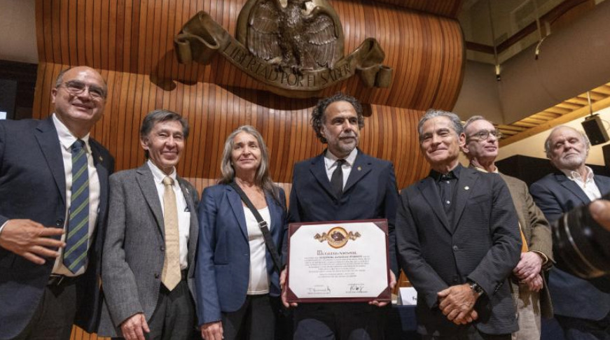 El cineasta Alejandro González Iñárritu al centro, sosteniendo su diploma oficial de ingreso, posa junto a miembros de El Colegio Nacional frente a un muro de madera con el escudo institucional tallado en la parte superior.