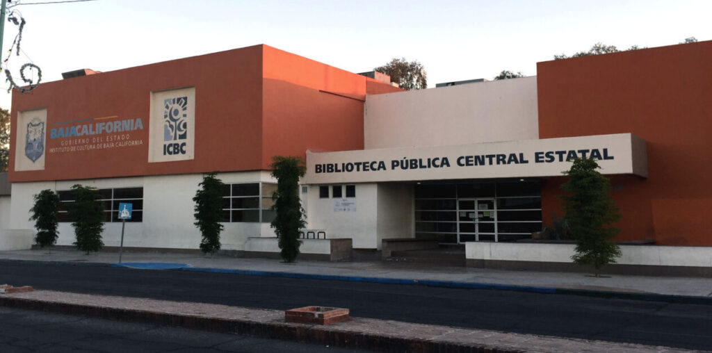 Fachada exterior de la Biblioteca Pública Central Estatal en Mexicali, Baja California, un edificio de color naranja con letreros oficiales del Gobierno del Estado.