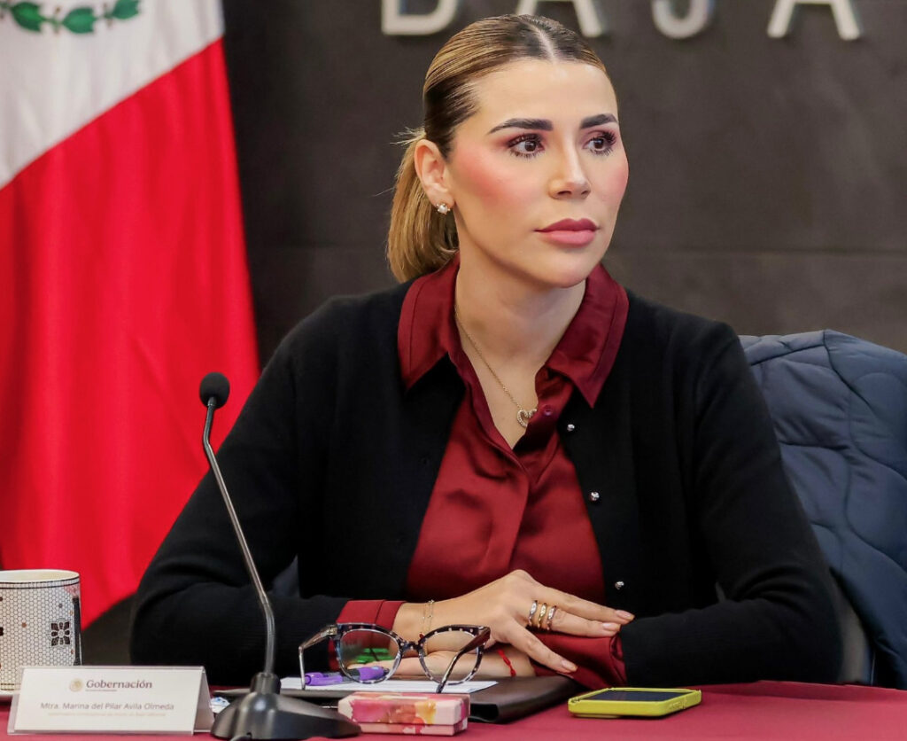 La gobernadora Marina del Pilar Ávila Olmeda sentada en una mesa de trabajo con la bandera de México al fondo, durante un pronunciamiento oficial.