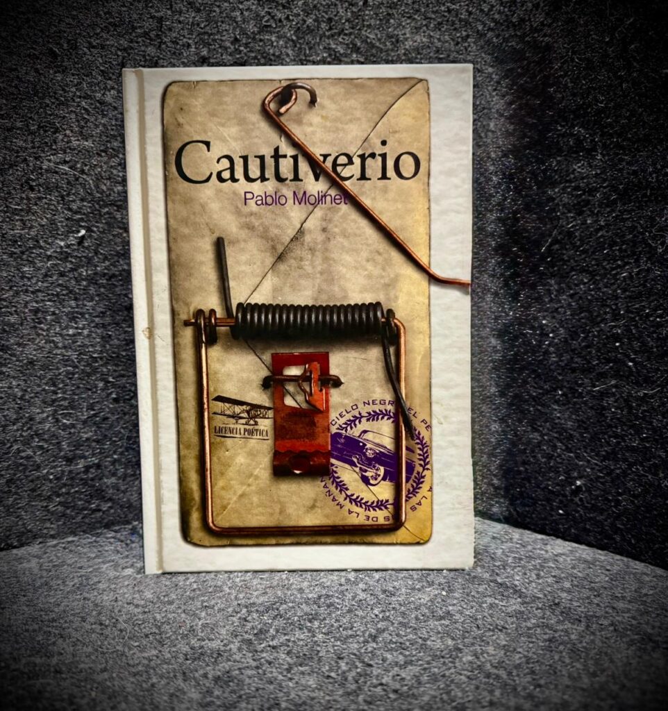 Fotografía en plano medio de la portada del libro Cautiverio de Pablo Molinet, editado por el Instituto Literario de Veracruz. El diseño de la portada, de tonos sepia y envejecidos, muestra la imagen de una trampa de alambre y madera, con un alambre real doblado que sobresale físicamente del borde del libro.