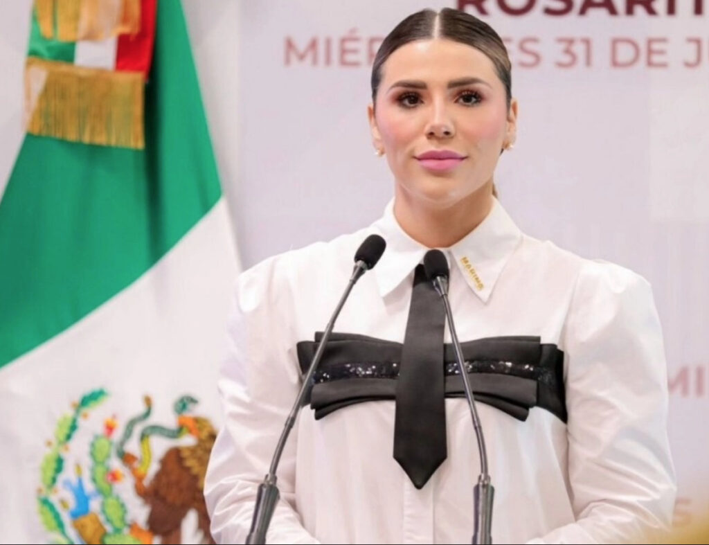 Retrato oficial en plano medio de la gobernadora de Baja California, Marina del Pilar Ávila Olmeda, sonriendo con el cabello recogido. Viste un saco formal de color claro frente a un fondo institucional difuminado.