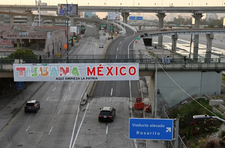 Perspectiva urbana de una avenida en Tijuana con un letrero peatonal que dice TIJUANA MÉXICO AQUÍ EMPIEZA LA PATRIA. En la parte inferior derecha se observa un señalamiento vial azul que indica el desvío hacia Viaducto elevado y Rosarito, rodeado por las estructuras de puentes superiores de concreto.