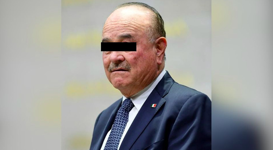 Fotografía oficial que documenta la detención de un hombre identificado como Ernesto Ruffo Appel, exgobernador de Baja California, de pie y flanqueado por dos agentes federales uniformados de la Fiscalía General de la República (FGR). El exmandatario viste una camisa formal de manga larga y pantalón oscuro, con una barra de censura negra cubriendo sus ojos para proteger sus derechos de identidad bajo el principio de presunción de inocencia. Los agentes a sus costados llevan uniformes tácticos oscuros con logotipos oficiales visibles de la corporación federal.
