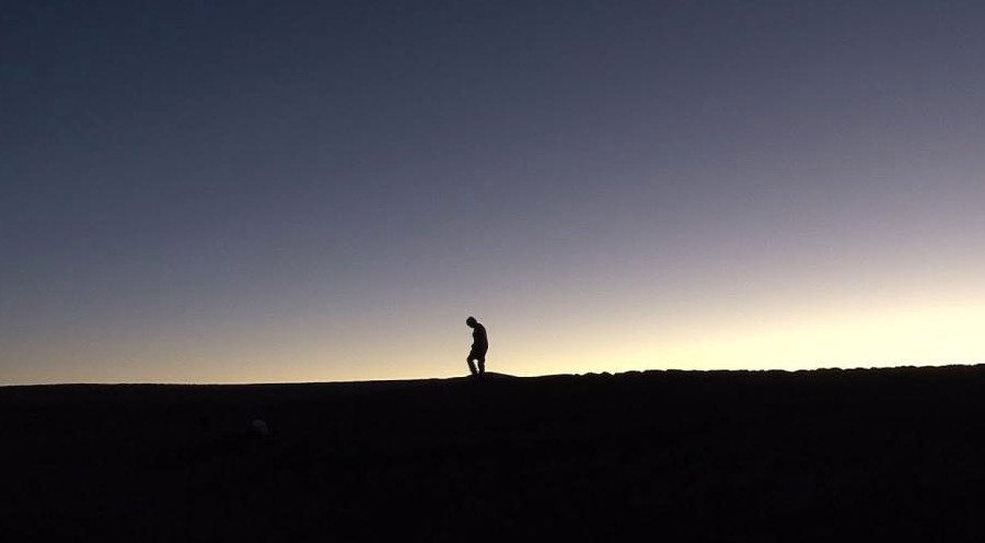 Silueta solitaria de una persona caminando sobre el horizonte en el desierto de Atacama durante el atardecer, fotograma del documental Nostalgia de la luz.