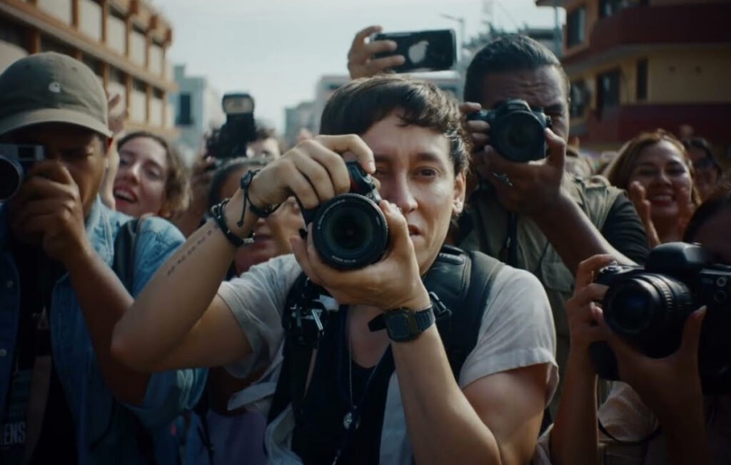 El actor mexicalense Hoze Meléndez en el centro sosteniendo una cámara fotográfica rodeado de fotoperiodistas en una escena de la película Cocodrilos.