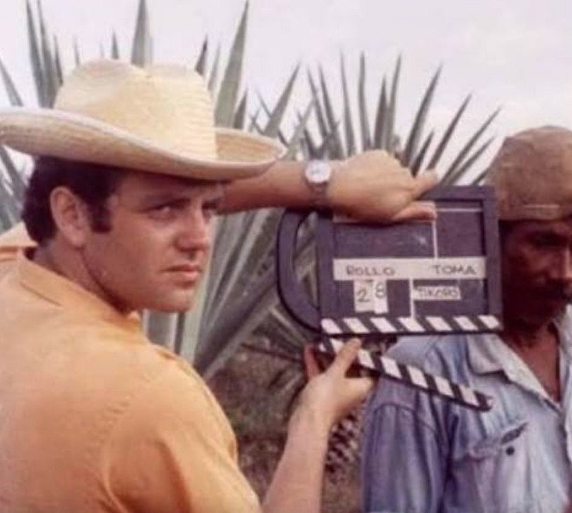 El cineasta Raymundo Gleyzer vistiendo sombrero de paja y sosteniendo una claustra de rodaje frente a plantas de maguey durante la filmación del documental México la revolución congelada.