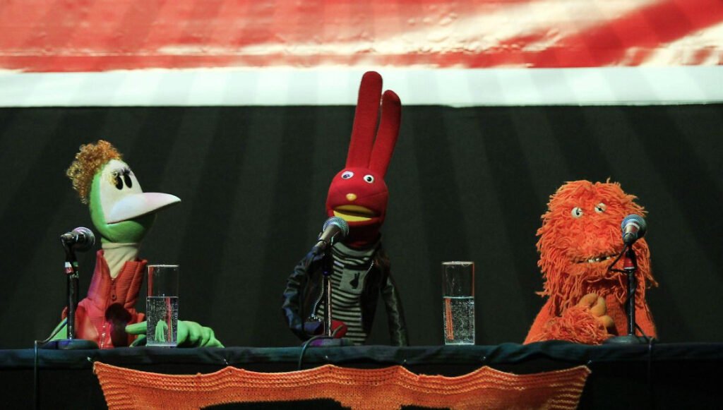 Títeres y marionetas de los personajes de 31 Minutos en un escenario con micrófonos durante una presentación en vivo.